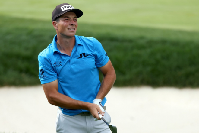 En golfspiller i blå skjorte, identifisert som PGA Tour-stjernen Viktor Hovland, ser intenst på banen til skuddet sitt på en solskinnsdag.