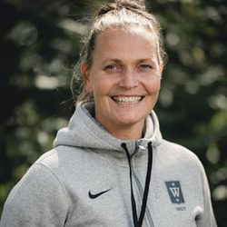En smilende kvinne, Grete Etholm, i en grå sports-hettegenser poserer utendørs.