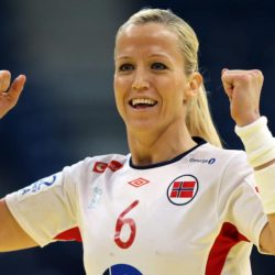 En kvinnelig idrettsutøver, Heidi Løke, i hvit og rød sportstrøye, med nummer 6, feirer med knyttet never og et gledelig uttrykk under et idrettsarrangement.