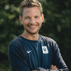 Trygg trener Fredrik Aukland med et vennlig smil poserer i sportsklær utendørs.
