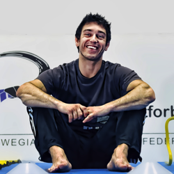 Den glade idrettsutøveren Mikael Flygind Larsen sitter på et gymnastikkapparat og bruker et øyeblikk på å smile og lade opp under trening.
