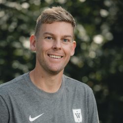 En smilende mann iført Nike sports-t-skjorte med uskarp bakgrunn av grønt løvverk er Stian Skjerven.