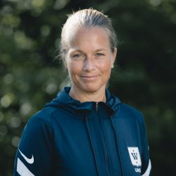 En selvsikker kvinnelig idrettsutøver, Linn-Therese Ugland Bekkevar, i sportsjakke med logo, utendørs med naturen i bakgrunnen.