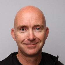 Smilende skallet mann med et vennlig uttrykk mot nøytral bakgrunn, kjent som Henning Lindanger.