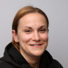 En smilende Laura Rollins med et subtilt glis, poserer for et bilde mot en nøytral grå bakgrunn.