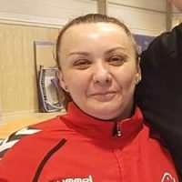 En kvinne i rød sportsjakke med logo, smiler lett til kameraet i en innendørs setting. - Madalina Tanase