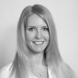 Et sort/hvitt hodebilde av Stine Cecilie Gålås smilende med langt hår, iført en lys bluse og et delikat halskjede.