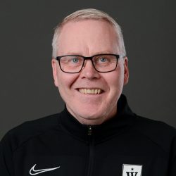 Portrett av en smilende Axel Stefansson med briller iført en svart sportsjakke med hvit logo.