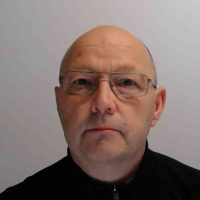 En skallet mann med briller iført svart skjorte, vendt mot kameraet med et nøytralt uttrykk, er Geir Mällberg.