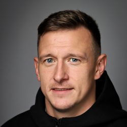 Portrett av Igor Kobiakov med kort hår, ser direkte på kameraet, iført en svart hettegenser mot en grå bakgrunn.