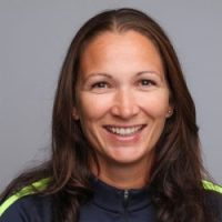 En smilende kvinne med langt hår, iført sporty antrekk, mot nøytral bakgrunn identifiseres som Kristine Wiig Skarlund.