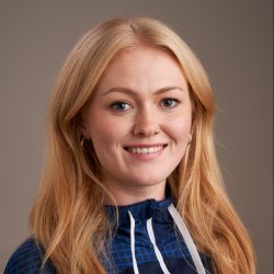 En smilende Marthe Mortensen Bjartveit med langt blondt hår, iført en blåmønstret topp, poserer for et profesjonelt portrett mot en nøytral bakgrunn.