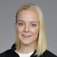 En smilende kvinne med blondt hår, iført svart topp, satt mot grå bakgrunn: Nathalie Brøndrup.
