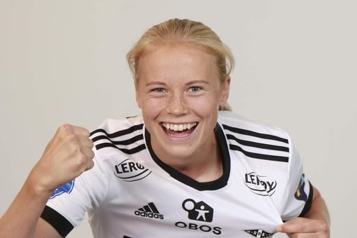 En glad fotballspiller, Julie Blakstad, i svart og hvit trøye, feirer triumferende med knyttnevepumpe og et lyst smil.
