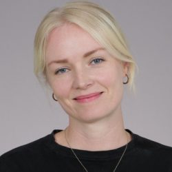 Et portrett av en smilende kvinne med blondt hår, subtil sminke og en svart topp, mot nøytral bakgrunn av Karine Furnes Eriksen.