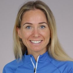 En smilende Kirsti Kolseth med langt blondt hår trukket tilbake, iført en blå glidelåstopp, mot nøytral bakgrunn.