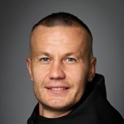 En mann med kort hår og et svakt smil, iført svart topp mot grå bakgrunn er Ståle Stålinho Sæthre.