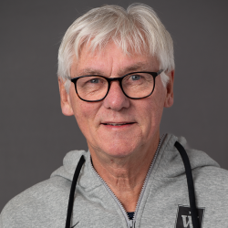 Et portrett av Åge Edvardsen, en smilende seniormann med hvitt hår, iført briller, og iført en grå hettegenser.