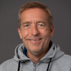 En smilende mann med grått hår, iført en grå hettegenser, med et varmt og vennlig uttrykk er Jan Kampenhøy.