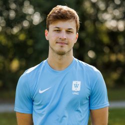 En selvsikker ung idrettsutøver, Magnus Knutsen, i en lyseblå sportstrøye står utendørs med et naturlig bakteppe, og utstråler besluttsomhet og fokus.