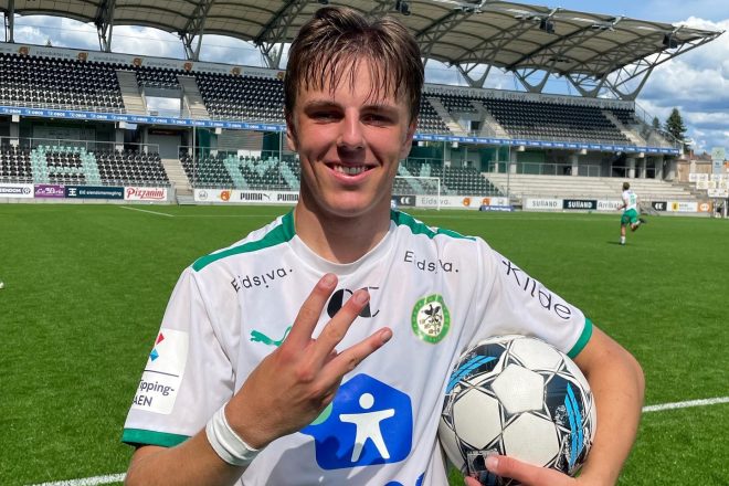 En glad fotballspiller, Julian Bakkeli Gonstad, viser frem matchballen med et stadion i bakgrunnen, trolig feiret et hat-trick eller en personlig prestasjon.