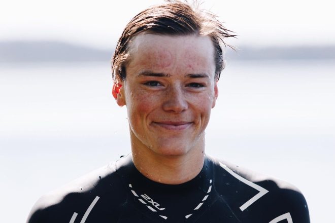 En ung idrettsutøver, Petter Ellingsbø, smiler til kameraet, frisk fra vannet med vått hår klistret til pannen, iført svart våtdrakt, legemliggjør ånden fra