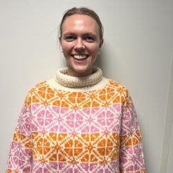 En smilende person, designet av Magdalena Ims, iført en turtleneck-genser med et intrikat oransje og hvitt mønster.