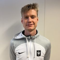 En smilende mann med kort blondt hår iført en grå sportsjakke med Nike-logo og et svart emblem med bokstaven "w" på venstre brystparti er Ludvik Mørk Johansen.