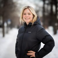 Selvsikker kvinne Maren Lundby i vinterjakke smiler utendørs på en snørik dag.
